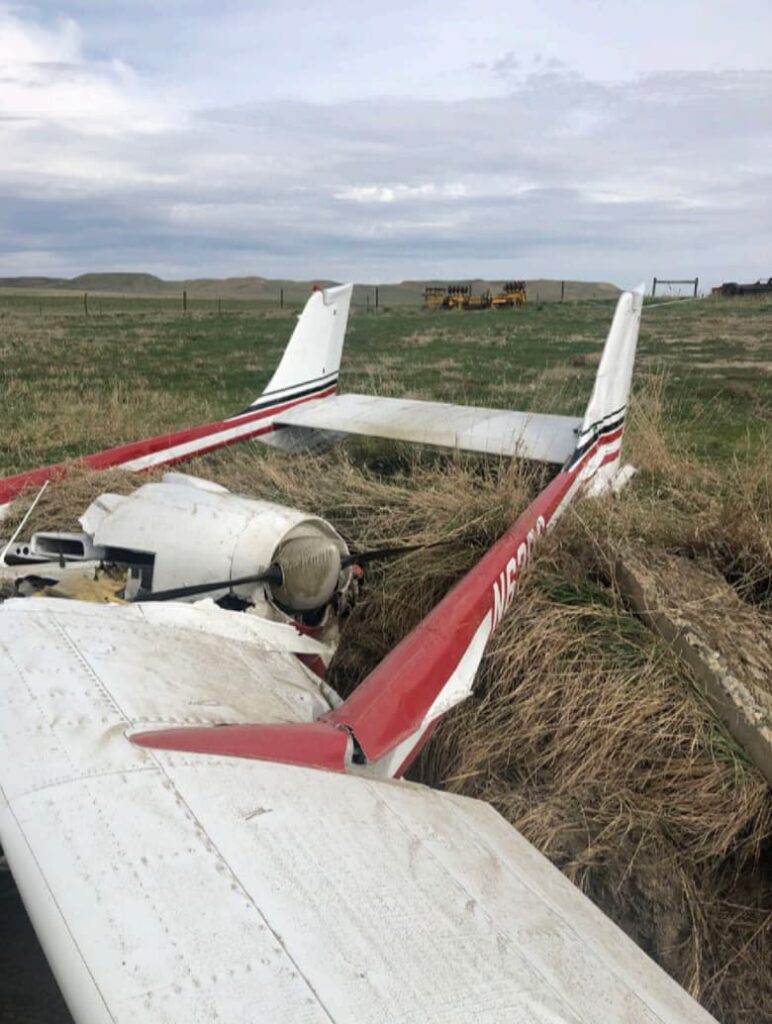 Rear view of Cessna P337H N62PC’s tail and rear engine nacelle in an irrigation ditch, with grass and farmland in the background under an overcast sky.